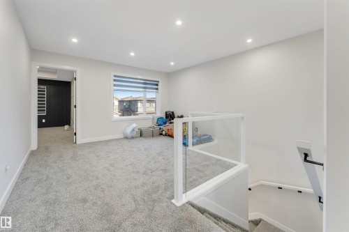 Spacious carpeted upper-level area featuring recessed lighting, a large window with horizontal blinds, and a modern glass panel railing system overlooking the staircase - 7007 169 Avenue Nw, Edmonton, AB - Indoor Photo Showing Other Room