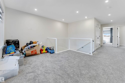 Spacious carpeted landing featuring recessed lighting, a contemporary glass and white railing, and multiple white paneled doors - 7007 169 Avenue Nw, Edmonton, AB - Indoor Photo Showing Other Room