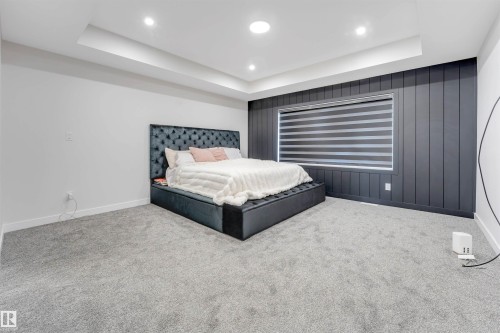 Spacious room featuring tray ceilings with recessed lighting, textured dark accent wall with a window, light gray carpeting, and white baseboards - 7007 169 Avenue Nw, Edmonton, AB - Indoor Photo Showing Bedroom