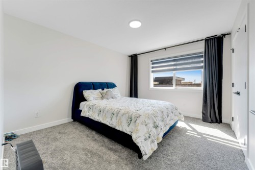 Bright room featuring a large window with roller shades and dark drapery, white walls, and gray carpet flooring - 7007 169 Avenue Nw, Edmonton, AB - Indoor Photo Showing Bedroom
