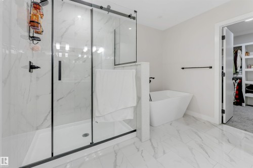 Spacious bathroom featuring a frameless glass shower enclosure with matte black hardware, a freestanding soaking tub, and large format marble-look tile flooring - 7007 169 Avenue Nw, Edmonton, AB - Indoor Photo Showing Bathroom