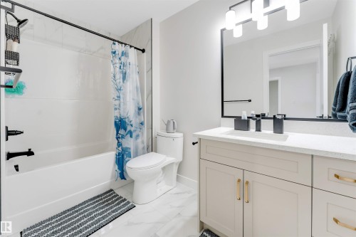 Bathroom featuring a white bathtub with a shower, a modern vanity with a white countertop and undermount sink, matte black fixtures, and a framed mirror with contemporary lighting - 7007 169 Avenue Nw, Edmonton, AB - Indoor Photo Showing Bathroom