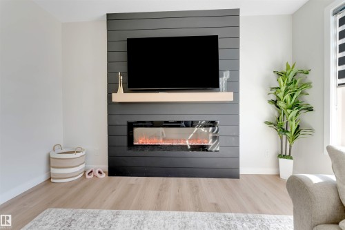 Media wall featuring horizontal shiplap paneling, a wall-mounted television, and a linear electric fireplace with a light wood-finish mantel - 7007 169 Avenue Nw, Edmonton, AB - Indoor Photo Showing Living Room With Fireplace