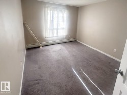 Carpeted room featuring a large window with vertical blinds, baseboard heating, and light-colored wall paint - 