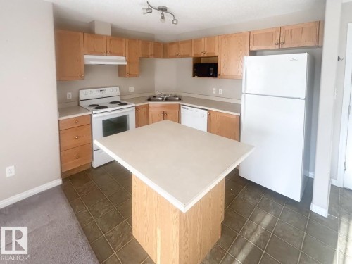 Kitchen featuring light wood cabinetry, white appliances, a center island with countertop, an integrated sink, and track lighting - 6120 7331 South Terwillegar Drive Nw, Edmonton, AB - Indoor Photo Showing Kitchen