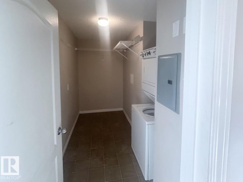 Dedicated laundry area featuring a stacked washer and dryer unit, overhead shelving, and neutral wall tones - 6120 7331 South Terwillegar Drive Nw, Edmonton, AB - Indoor