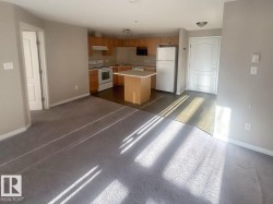 Open-concept living area with gray carpeting transitioning to wood-finish flooring in the kitchen - 