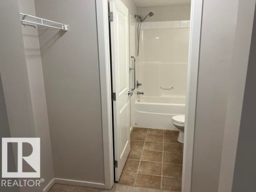 Bathroom featuring a white bathtub and shower combination with an integrated grab bar, tile flooring, and a white toilet - 118 3357 16A Avenue, Edmonton, AB 