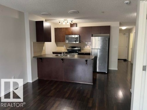 Kitchen featuring dark wood-finish cabinetry, stainless steel appliances, a breakfast bar, recessed lighting, and dark wood-finish flooring - 118 3357 16A Avenue, Edmonton, AB 