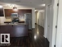 Kitchen featuring dark wood-finish cabinetry, stainless steel appliances, a subway tile backsplash, and a central island with an integrated sink - 118 3357 16A Avenue, Edmonton, AB 