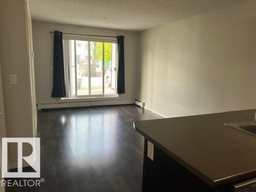 Spacious interior featuring dark wood-finish flooring, light-toned walls, and a sliding glass door providing natural light - 118 3357 16A Avenue, Edmonton, AB 