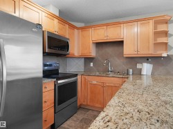 Kitchen featuring wood cabinetry, stainless steel appliances, a tile backsplash, granite countertops, and a stainless steel sink with a gooseneck faucet - 