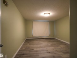 Spacious room featuring wood-finish flooring, light green walls, white trim, and a window with a roller shade - 