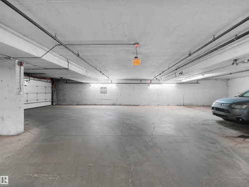 Spacious concrete floor parking area featuring fluorescent lighting, exposed pipework, and a white roll-up garage door - 7123 7327 South Terwillegar Drive, Edmonton, AB - Indoor Photo Showing Garage