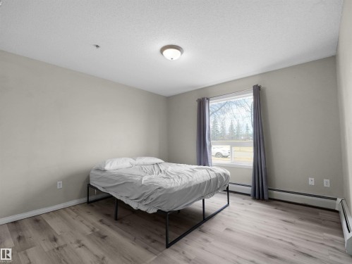 Spacious room featuring wood-finish flooring, a large window with vertical blinds, and a flush-mount ceiling light fixture - 7123 7327 South Terwillegar Drive, Edmonton, AB - Indoor Photo Showing Bedroom