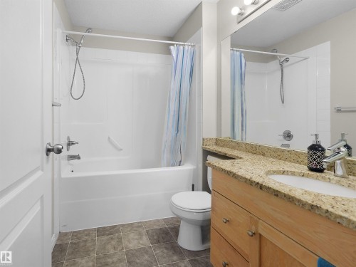 Bathroom featuring a built-in tub with shower, a light wood-finish vanity with a stone countertop, an integrated sink, and square floor tiles - 7123 7327 South Terwillegar Drive, Edmonton, AB - Indoor Photo Showing Bathroom