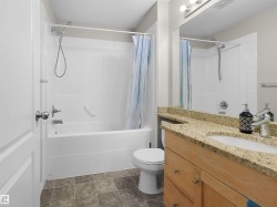 Bathroom featuring a built-in tub with shower, a light wood-finish vanity with a stone countertop, an integrated sink, and square floor tiles - 