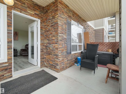 Expansive covered patio featuring a stacked stone exterior, concrete flooring, and a white framed glass-panel door - 7123 7327 South Terwillegar Drive, Edmonton, AB - Outdoor With Exterior