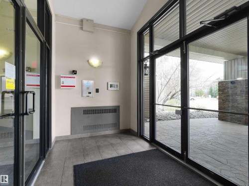 Entryway featuring large glass doors with black framing, tiled flooring, and a wall-mounted intercom system - 7123 7327 South Terwillegar Drive, Edmonton, AB - Indoor Photo Showing Other Room