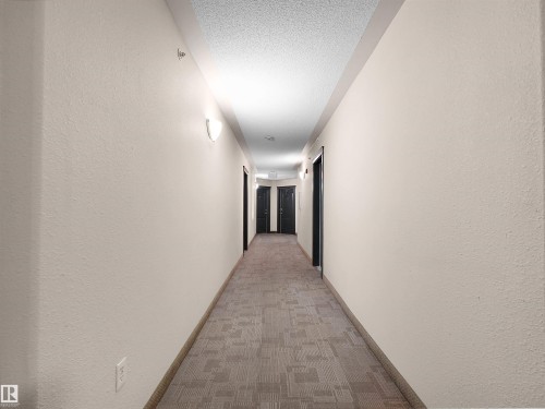 Well-lit interior hallway featuring patterned carpeting and multiple entry doors - 7123 7327 South Terwillegar Drive, Edmonton, AB - Indoor Photo Showing Other Room