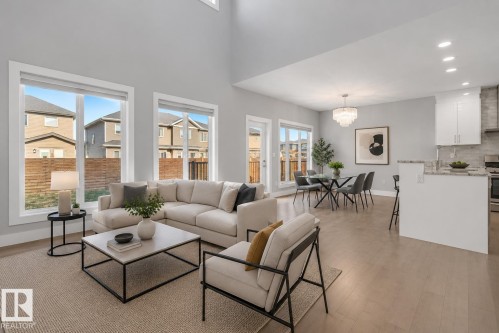 Open-concept living space featuring high ceilings, light wood-finish flooring, and large windows. Virtually Staged. - 635 42 Street, Edmonton, AB - Indoor Photo Showing Living Room