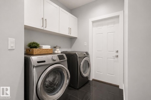 Utility area with dark tile flooring, white shaker-style cabinetry, and a paneled door with brushed nickel hardware. Virtually Staged. - 635 42 Street, Edmonton, AB - Indoor Photo Showing Laundry Room