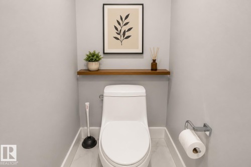 Contemporary powder room featuring a sleek white toilet, light gray walls, and a wood-finish floating shelf. Virtually Staged. - 635 42 Street, Edmonton, AB - Indoor Photo Showing Bathroom
