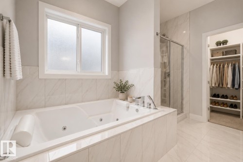 Bathroom featuring a built-in jetted tub with polished chrome fixtures, a glass-enclosed shower, and large format white tile flooring and wall accents. Virtually Staged. - 635 42 Street, Edmonton, AB - Indoor Photo Showing Bathroom