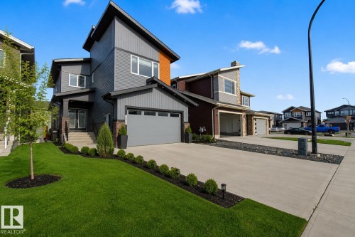 Contemporary multi-level residence featuring gray siding, a triple tandem garage, and a concrete driveway. Grass virtually enhanced to give a summer look. - 635 42 Street, Edmonton, AB - Outdoor With Facade