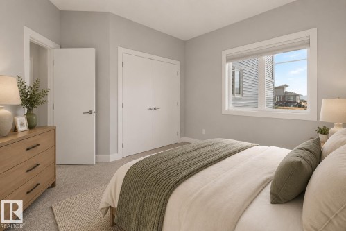 Carpeted bedroom featuring a double-pane window, white trim throughout, and two white bi-fold closet doors. Virtually Staged. - 635 42 Street, Edmonton, AB - Indoor Photo Showing Bedroom