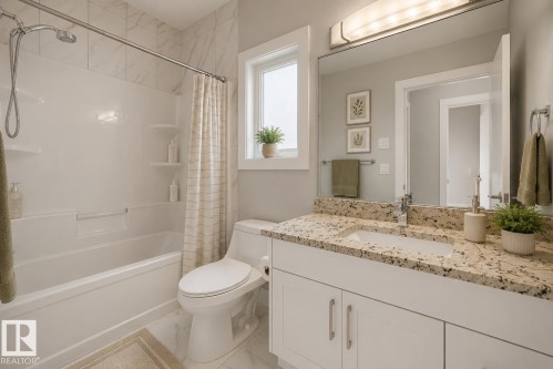 Bathroom featuring a built-in tub with a shower fixture, wall-mounted vanity with an undermount sink, granite-style countertop, and a window for natural light. Virtually Staged. - 635 42 Street, Edmonton, AB - Indoor Photo Showing Bathroom