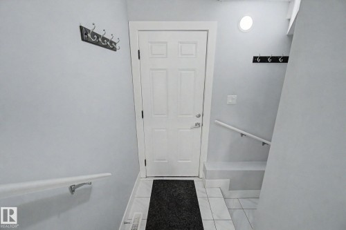Entryway featuring a paneled door with polished hardware, white tile flooring, and white painted walls. - 635 42 Street, Edmonton, AB - Indoor Photo Showing Other Room