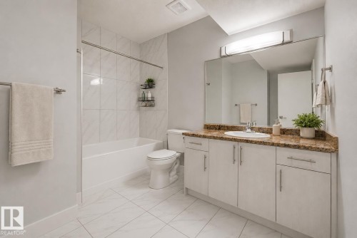 Bathroom featuring a white bathtub with subway tile surround, a white toilet, and a vanity with a light brown stone countertop, undermount sink, and white cabinetry. Virtually Staged. - 635 42 Street, Edmonton, AB - Indoor Photo Showing Bathroom