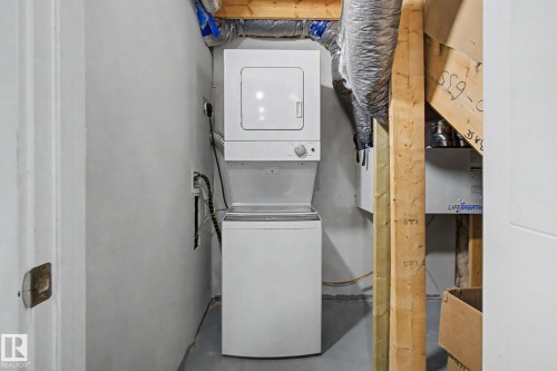 Dedicated laundry area featuring a white stacked washer and dryer unit, exposed wooden beams, and ductwork - 635 42 Street, Edmonton, AB - Indoor Photo Showing Laundry Room