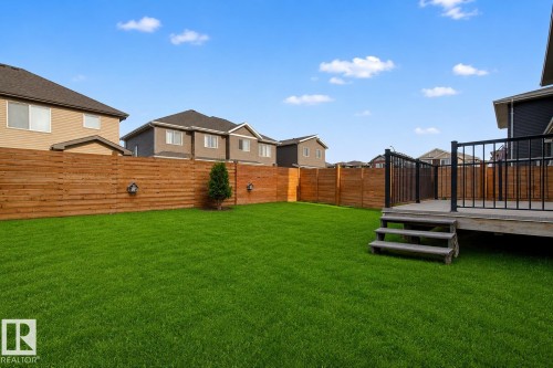 Expansive green lawn with a wood plank privacy fence and integrated wall-mounted lighting. Lawn enhanced for summer look. - 635 42 Street, Edmonton, AB - Outdoor
