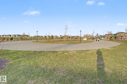 Paved pathway through a green space featuring integrated lighting fixtures, a distant playground structure, and residential architecture bordering the parkland - 635 42 Street, Edmonton, AB - Outdoor With View