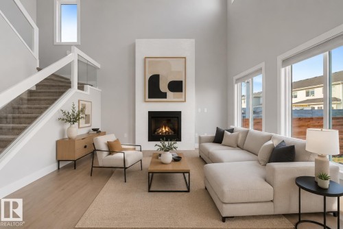 Two-story living area featuring a fireplace with a white surround, tall ceilings, and large windows. Virtually Staged. - 635 42 Street, Edmonton, AB - Indoor Photo Showing Living Room With Fireplace