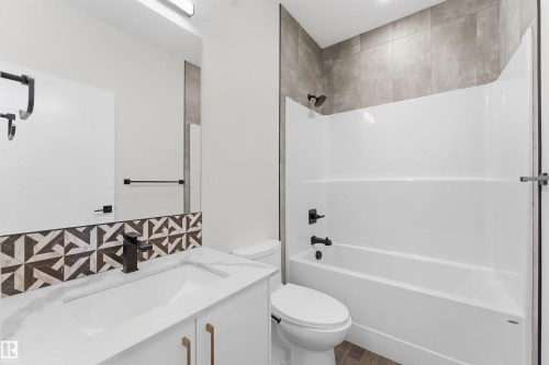 Bathroom featuring a vanity with a white countertop and integrated sink, a patterned tile backsplash, and a large mirror - 12447 47 Street, Edmonton, AB - Indoor Photo Showing Bathroom