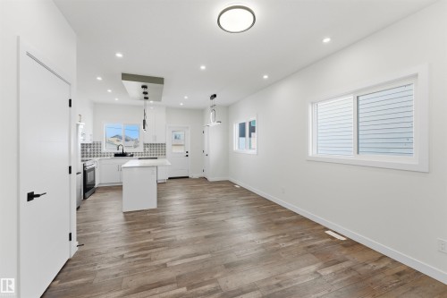 Bright open-concept living area featuring wood-finish flooring, white walls, recessed lighting, a modern kitchen island, and a geometric tile backsplash - 12447 47 Street, Edmonton, AB - Indoor Photo Showing Other Room