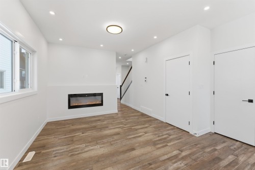 Living area featuring a modern electric fireplace, wood-finish flooring, recessed lighting, and a contemporary ceiling fixture - 12447 47 Street, Edmonton, AB - Indoor With Fireplace