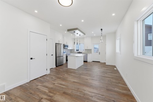 Open-concept kitchen and dining area featuring wood-finish flooring, white cabinetry, stainless steel appliances, a center island with pendant lighting, and recessed ceiling lights - 12447 47 Street, Edmonton, AB - Indoor Photo Showing Other Room
