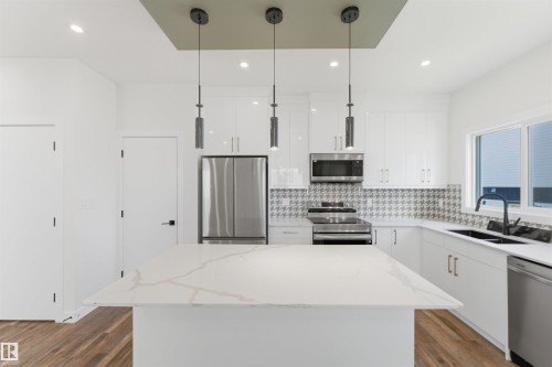 Kitchen featuring a large central island with a light-toned countertop, white cabinetry with silver hardware, full suite of stainless steel appliances, and a patterned backsplash - 12447 47 Street, Edmonton, AB - Indoor Photo Showing Kitchen With Stainless Steel Kitchen With Double Sink With Upgraded Kitchen