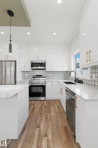 Modern kitchen featuring white cabinetry, stainless steel appliances, wood-finish flooring, white countertops, and a patterned backsplash - 12447 47 Street, Edmonton, AB - Indoor Photo Showing Kitchen With Stainless Steel Kitchen With Upgraded Kitchen