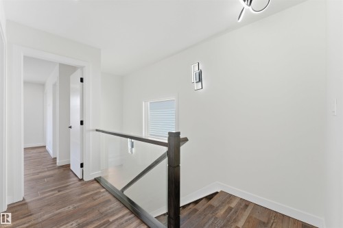 Upper-level hallway featuring wood-finish flooring, white walls, and a contemporary glass and dark wood railing - 12447 47 Street, Edmonton, AB - Indoor Photo Showing Other Room