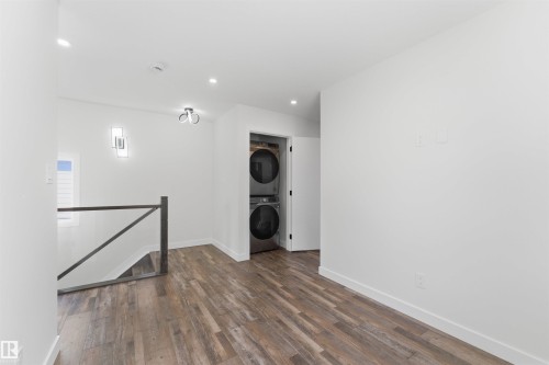 Laundry area featuring stacked appliances, wood-finish flooring, recessed lighting, and a contemporary ceiling fixture - 12447 47 Street, Edmonton, AB - Indoor Photo Showing Other Room