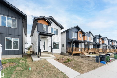 Contemporary exterior with white siding and dark grey accents, featuring a covered entry, concrete walkway, and multiple window placements - 12447 47 Street, Edmonton, AB - Outdoor With Facade
