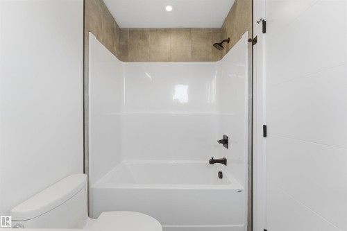 Bathroom featuring a white bathtub and shower unit with dark-finished fixtures, a white toilet, and a recessed ceiling light - 12447 47 Street, Edmonton, AB - Indoor Photo Showing Bathroom