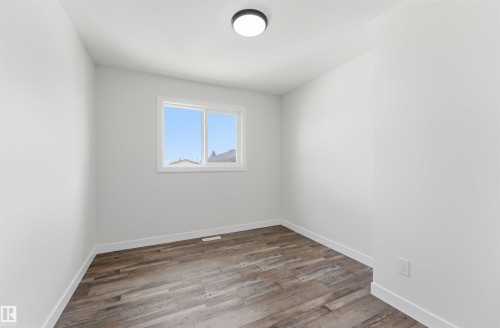Bright room featuring wood-finish flooring, white baseboards, a dual-pane window, and a flush-mount ceiling light fixture - 12447 47 Street, Edmonton, AB - Indoor Photo Showing Other Room