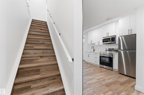 Contemporary kitchen featuring white cabinetry, stainless steel appliances, a matte black faucet, and wood-finish flooring - 12447 47 Street, Edmonton, AB - Indoor Photo Showing Kitchen With Stainless Steel Kitchen