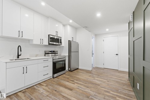Contemporary kitchen area featuring white cabinetry, stainless steel appliances, a black pull-down faucet, and wood-finish flooring - 12447 47 Street, Edmonton, AB - Indoor Photo Showing Kitchen With Stainless Steel Kitchen With Upgraded Kitchen